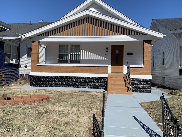 bungalow featuring covered porch, brick siding, and fence