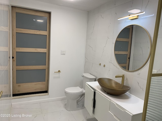 bathroom featuring tile walls, marble finish floor, vanity, and toilet