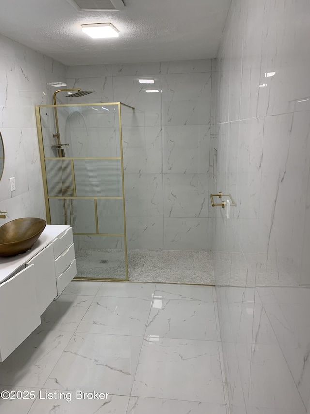 bathroom with vanity, a tile shower, and a textured ceiling