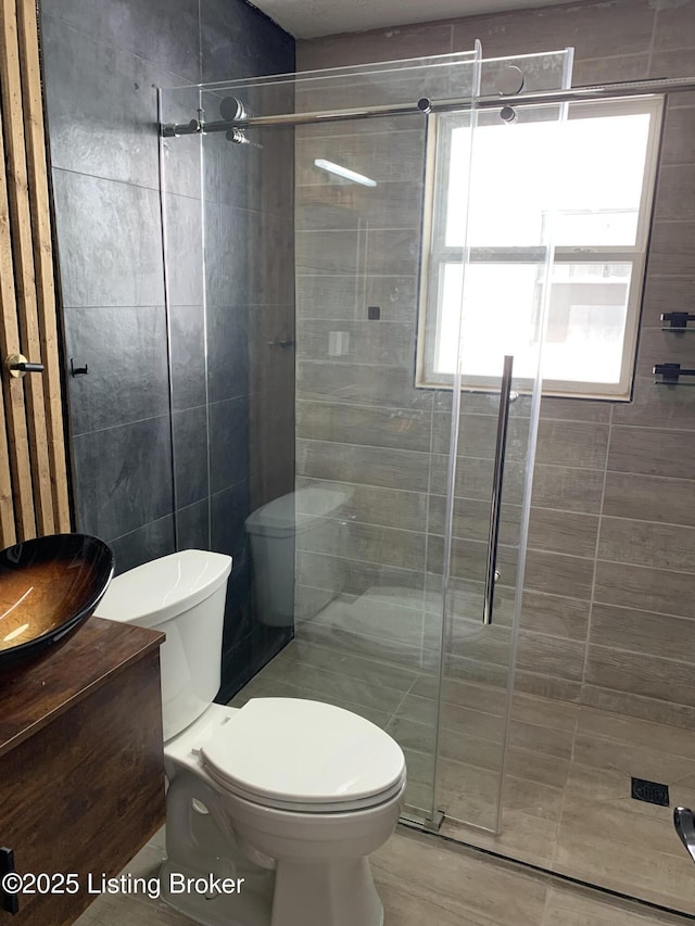 bathroom with tile walls, a shower stall, toilet, and vanity