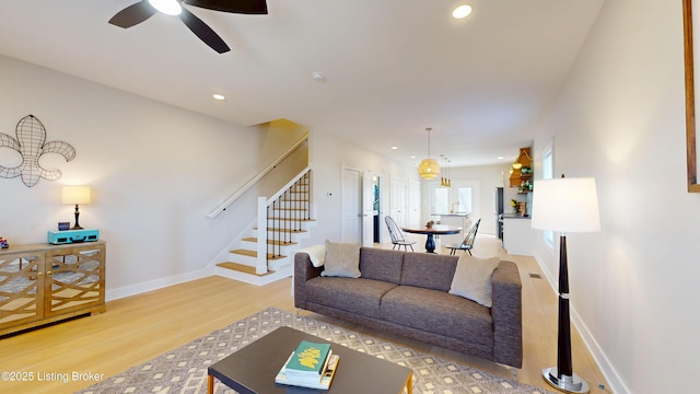 living room with ceiling fan, light wood-style flooring, recessed lighting, baseboards, and stairway