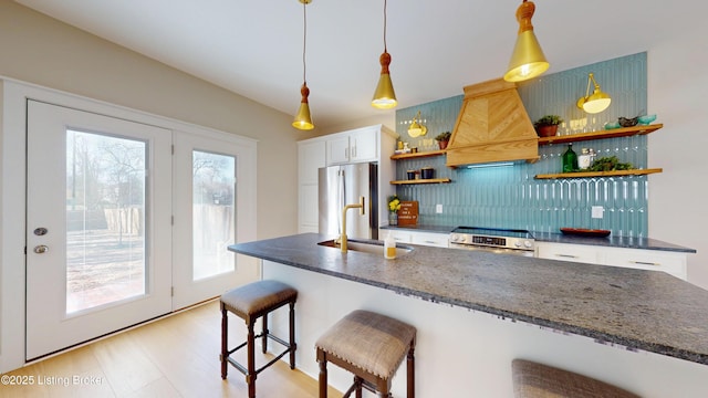 kitchen featuring a breakfast bar, custom exhaust hood, open shelves, stainless steel appliances, and white cabinetry