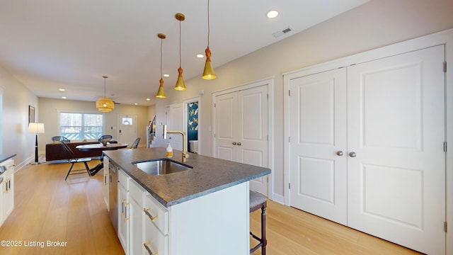 kitchen with visible vents, a sink, a kitchen island with sink, and white cabinets