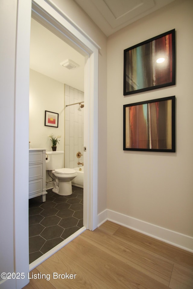 bathroom with toilet, wood finished floors, bathing tub / shower combination, visible vents, and baseboards