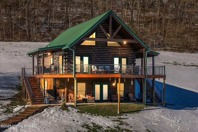 snow covered rear of property with a wooden deck and french doors