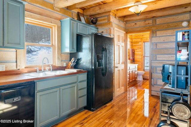 kitchen featuring butcher block countertops, sink, black appliances, beam ceiling, and light hardwood / wood-style flooring