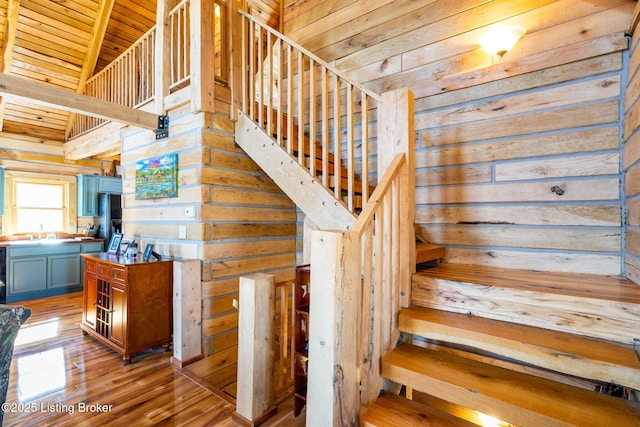 stairs with hardwood / wood-style floors, a towering ceiling, wooden ceiling, and wood walls