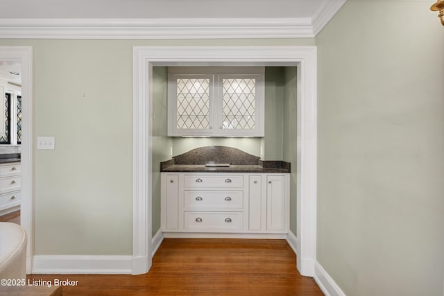 interior space with hardwood / wood-style flooring, crown molding, white cabinets, and dark stone counters