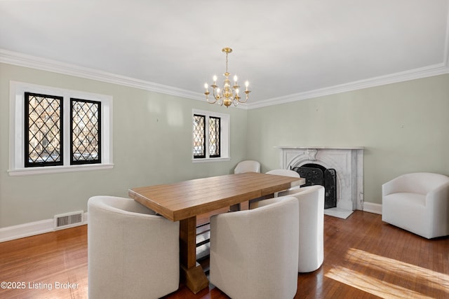 dining space featuring wood-type flooring, ornamental molding, an inviting chandelier, and a high end fireplace