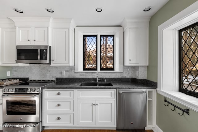 kitchen featuring appliances with stainless steel finishes, tasteful backsplash, white cabinetry, sink, and dark stone countertops