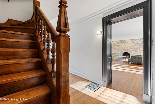 staircase featuring ornamental molding, a stone fireplace, and hardwood / wood-style floors