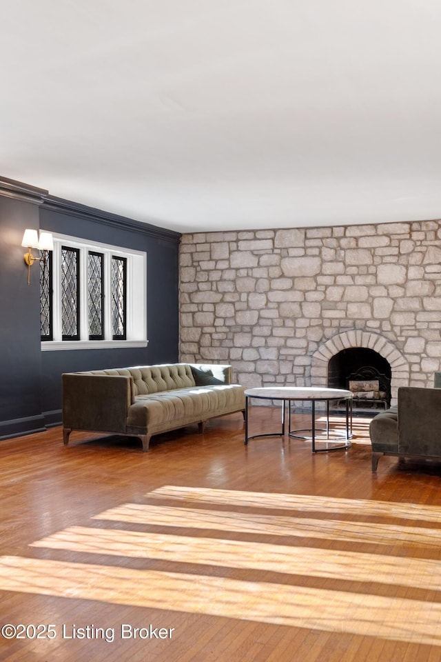 living room with wood-type flooring, a stone fireplace, and crown molding