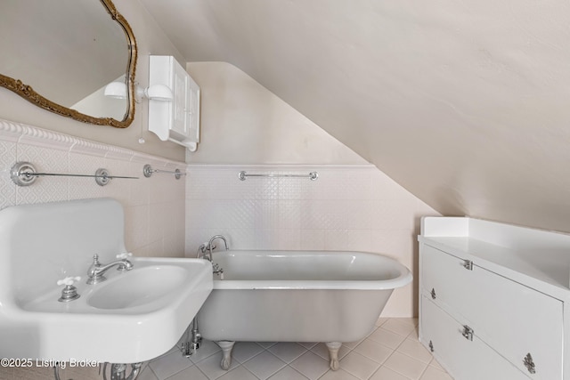 bathroom with a washtub, sink, tile patterned flooring, tile walls, and vaulted ceiling