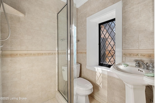 bathroom with tile walls, sink, a shower with shower door, and toilet