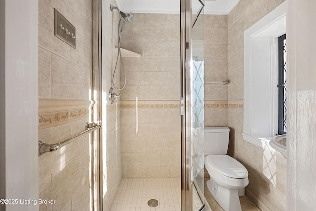 bathroom featuring a shower with door, ornamental molding, tile walls, and toilet