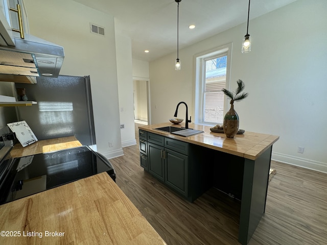 kitchen featuring stainless steel refrigerator, decorative light fixtures, a kitchen island with sink, and sink