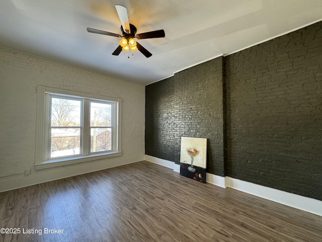 unfurnished room featuring hardwood / wood-style floors, ceiling fan, and brick wall