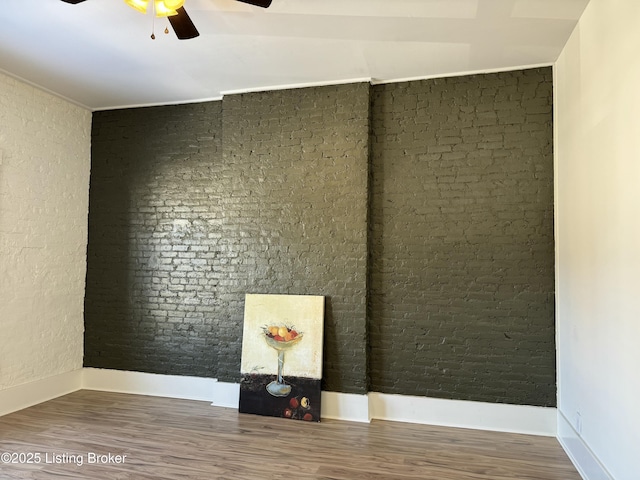 spare room featuring hardwood / wood-style flooring, ceiling fan, and brick wall