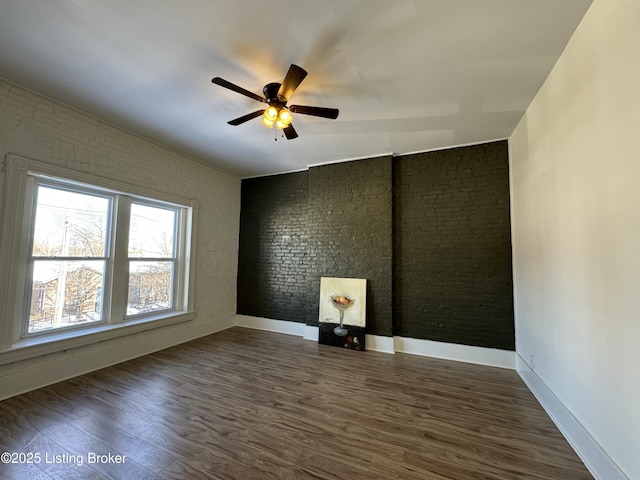 empty room with brick wall, dark wood-type flooring, and ceiling fan