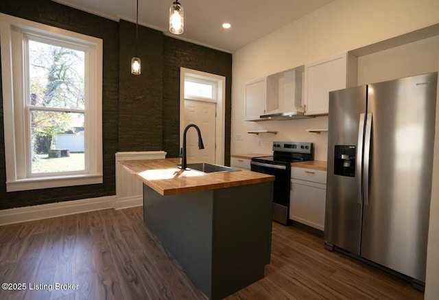 kitchen featuring hanging light fixtures, stainless steel appliances, an island with sink, white cabinets, and wall chimney exhaust hood