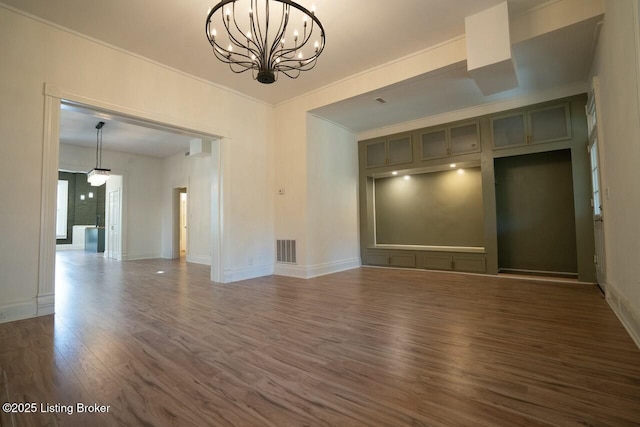 empty room featuring dark wood-type flooring, crown molding, and a chandelier