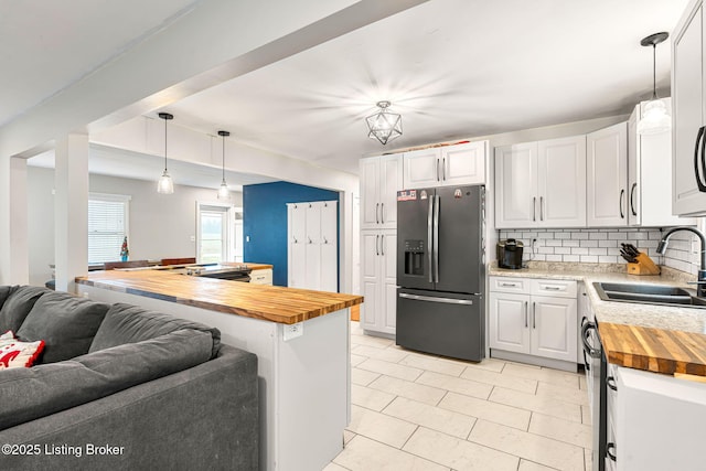 kitchen with stainless steel refrigerator with ice dispenser, sink, butcher block countertops, hanging light fixtures, and white cabinets