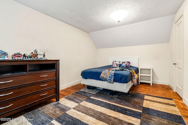 bedroom featuring vaulted ceiling, dark hardwood / wood-style floors, and a textured ceiling