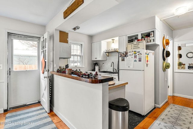 kitchen with sink, white cabinetry, wood-type flooring, kitchen peninsula, and white fridge