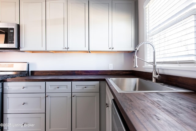 kitchen with wood counters, appliances with stainless steel finishes, sink, and gray cabinetry