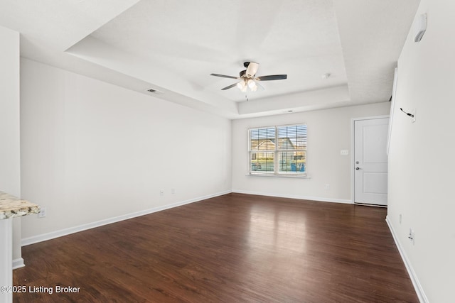 interior space with dark wood-style floors, a tray ceiling, ceiling fan, and baseboards