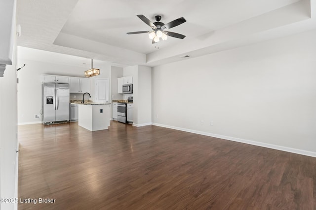 unfurnished living room featuring a tray ceiling, dark wood-style flooring, a sink, ceiling fan, and baseboards