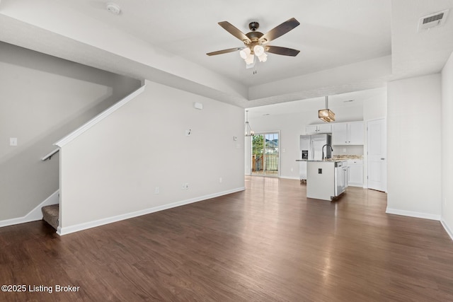 unfurnished living room with visible vents, baseboards, ceiling fan, stairway, and dark wood-style flooring