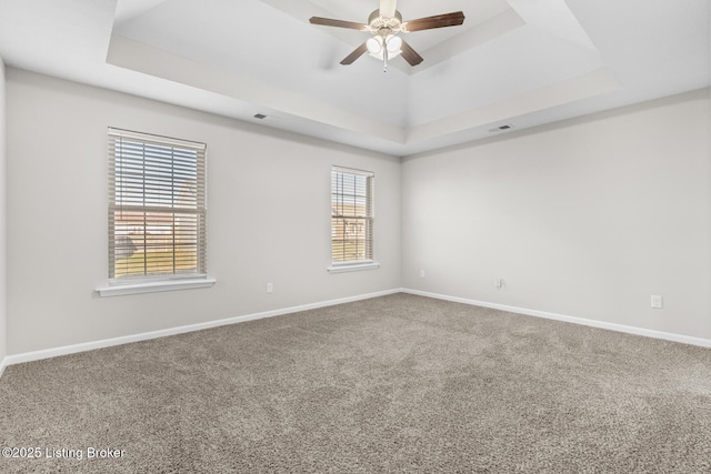 empty room with carpet floors, visible vents, baseboards, a ceiling fan, and a raised ceiling