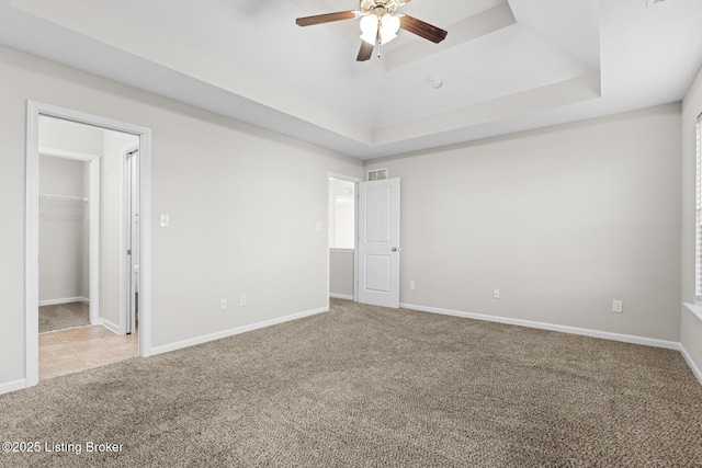 unfurnished bedroom featuring baseboards, a raised ceiling, ceiling fan, carpet, and a walk in closet