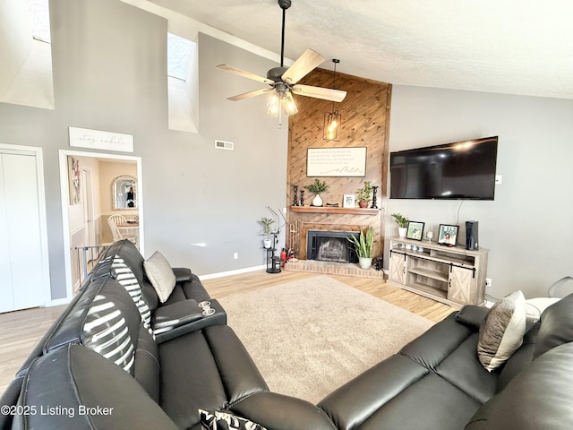 living room with high vaulted ceiling, a textured ceiling, ceiling fan, a fireplace, and light hardwood / wood-style floors