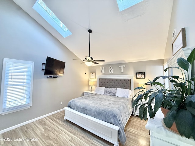 bedroom featuring high vaulted ceiling, a skylight, light hardwood / wood-style floors, and ceiling fan