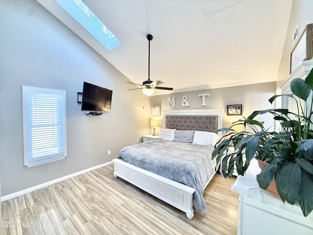 bedroom with ceiling fan, a skylight, high vaulted ceiling, and light wood-type flooring