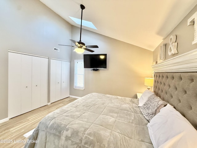 bedroom featuring ceiling fan, two closets, wood-type flooring, and vaulted ceiling with skylight