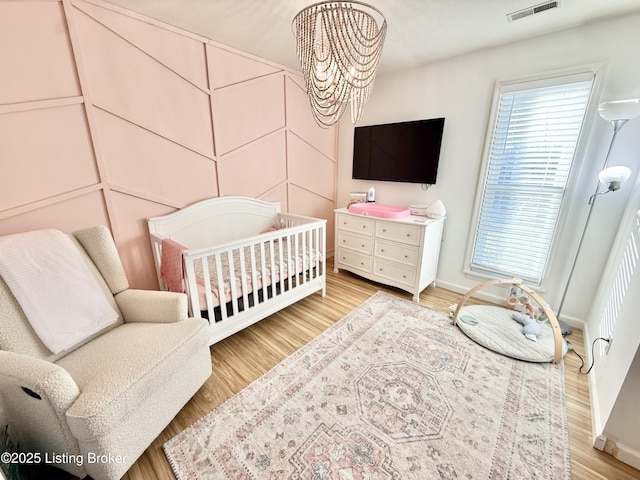 bedroom featuring a chandelier, light hardwood / wood-style floors, and a crib