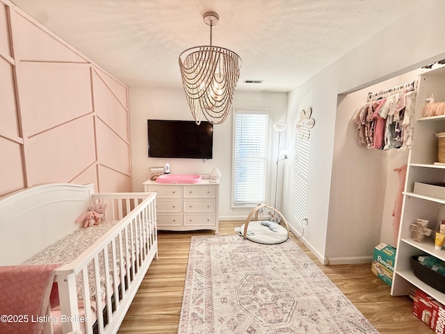 bedroom with a notable chandelier, a crib, a textured ceiling, and light hardwood / wood-style floors