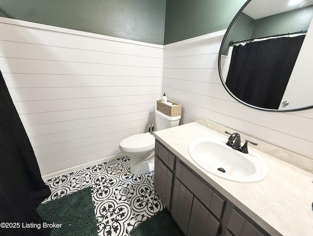 bathroom with wood walls, vanity, tile patterned floors, and toilet