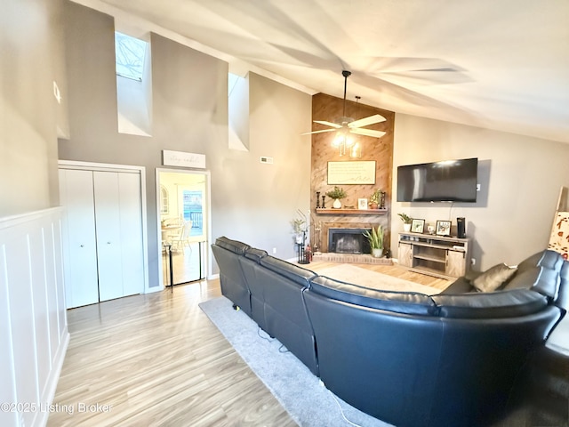 living room featuring ceiling fan, high vaulted ceiling, a fireplace, and light hardwood / wood-style flooring