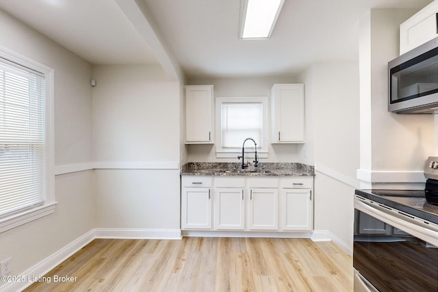 kitchen with sink, light hardwood / wood-style flooring, stone counters, white cabinetry, and appliances with stainless steel finishes