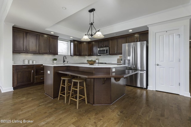 kitchen with a kitchen island, dark brown cabinetry, a tray ceiling, appliances with stainless steel finishes, and dark wood-style floors