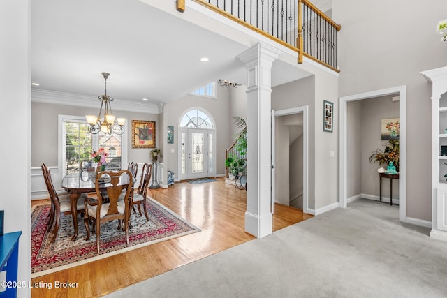 dining space with baseboards, ornamental molding, wood finished floors, a high ceiling, and ornate columns