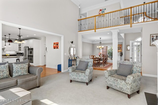 living area with crown molding, a notable chandelier, ornate columns, a towering ceiling, and baseboards