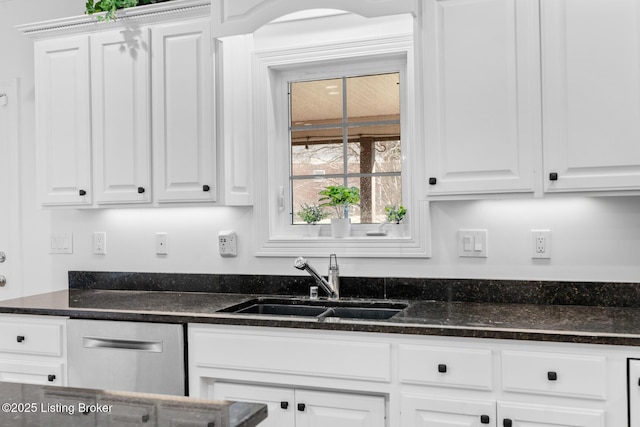 kitchen with dark stone countertops, a sink, and white cabinetry