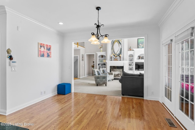 interior space featuring visible vents, a glass covered fireplace, wood finished floors, and ornamental molding