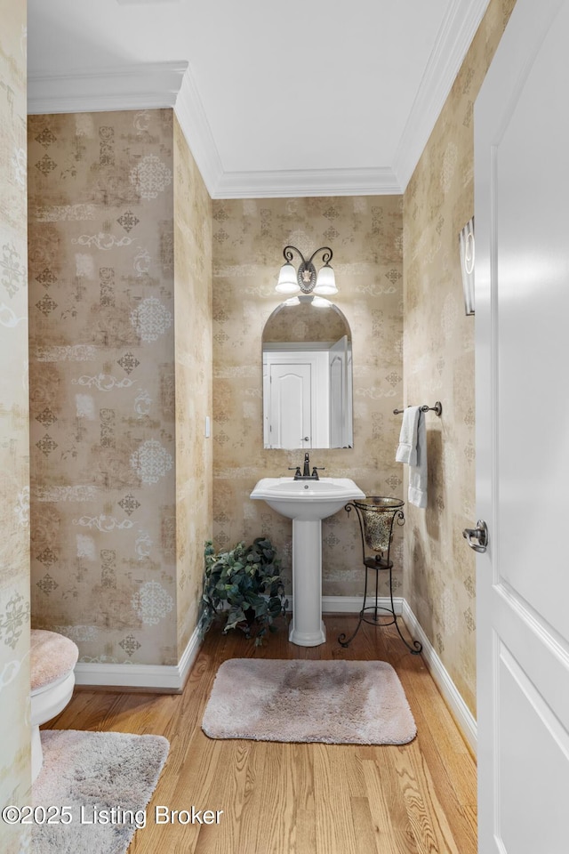 half bath featuring wallpapered walls, crown molding, and wood finished floors