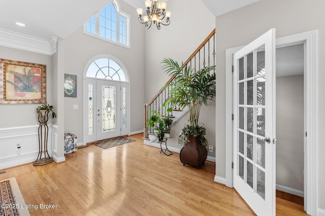 foyer with baseboards, stairway, wood finished floors, crown molding, and a notable chandelier